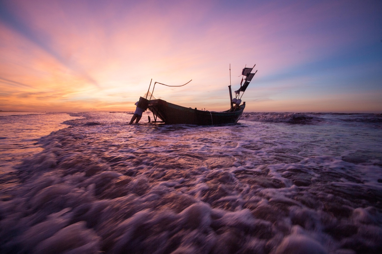 Un pescador empujando su lancha al agua al atardecer